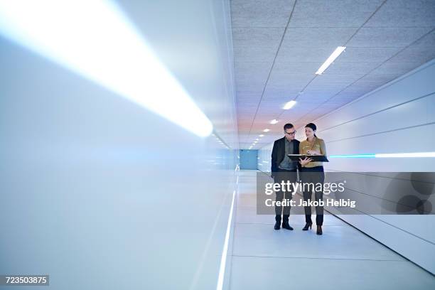 businesswoman and man reading file in office corridor - actualización comunicación fotografías e imágenes de stock