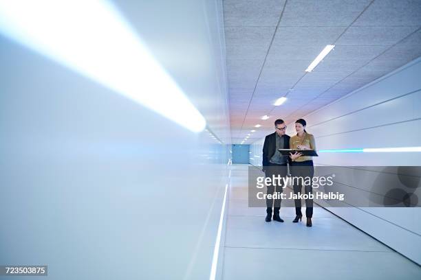businesswoman and man reading file in office corridor - business man woman walking stock pictures, royalty-free photos & images