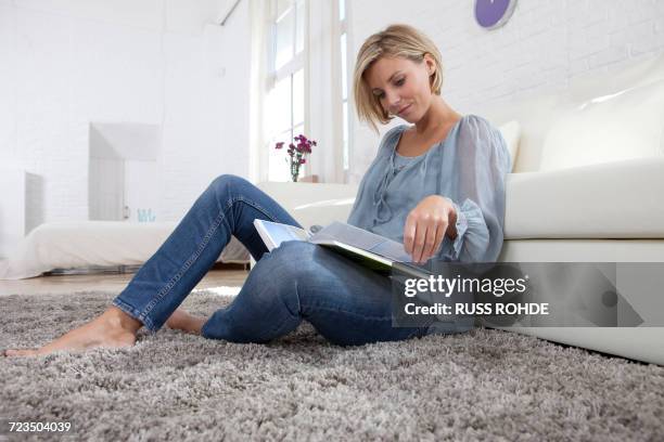 mid adult woman sitting on rug reading book - sitting on ground stock pictures, royalty-free photos & images