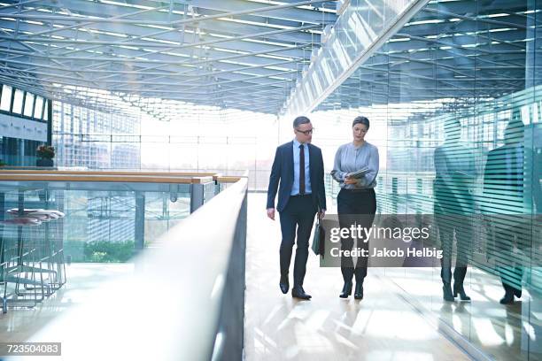 businessman and woman walking and talking on office balcony - actualización comunicación fotografías e imágenes de stock