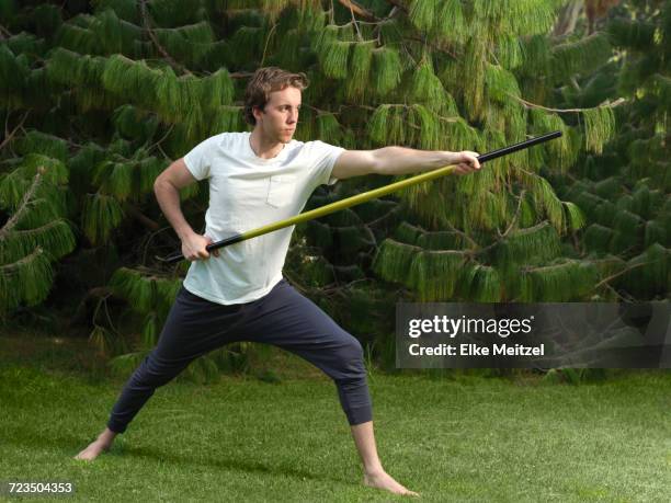 poised young man in park practicing martial arts holding bo staff - farbharmonie stock-fotos und bilder