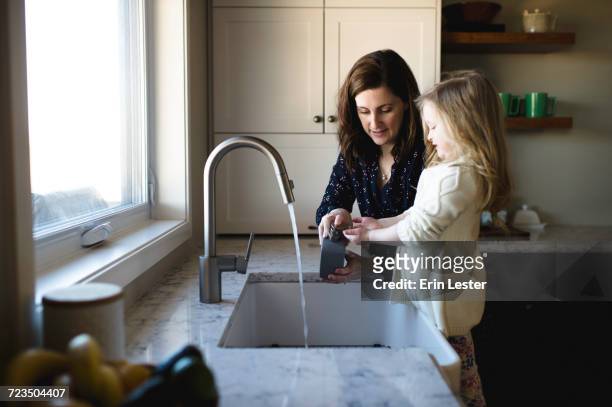 woman helping daughter wash hands at kitchen sink - child washing hands stockfoto's en -beelden