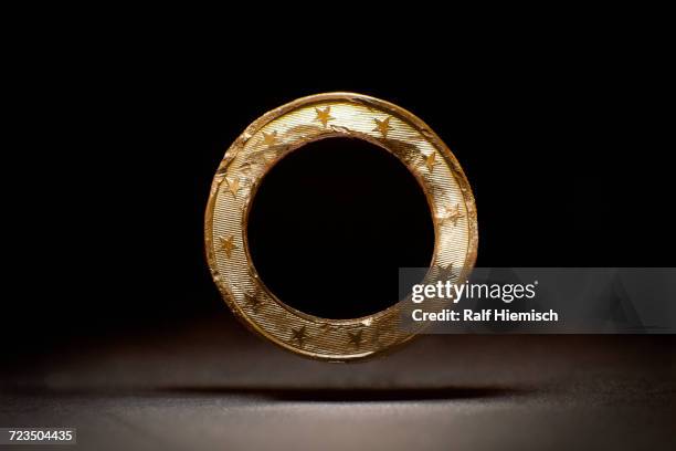 damaged metal of euro coin levitating against black background - euro star stock pictures, royalty-free photos & images