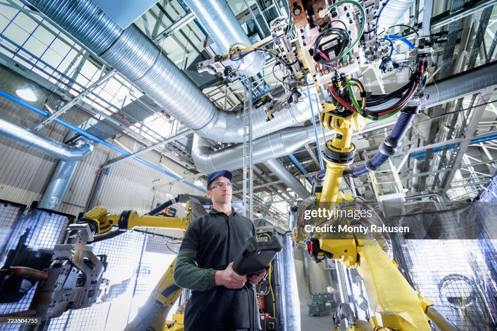 Apprentice engineer adjusting robot in car factory