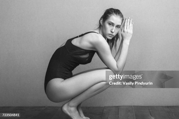 side view portrait of woman wearing leotard while crouching on hardwood floor against wall - human body foto e immagini stock