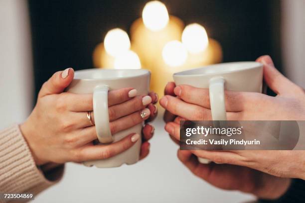 cropped image of couple holding coffee cups against illuminated candles at home - christmas coffee stock pictures, royalty-free photos & images