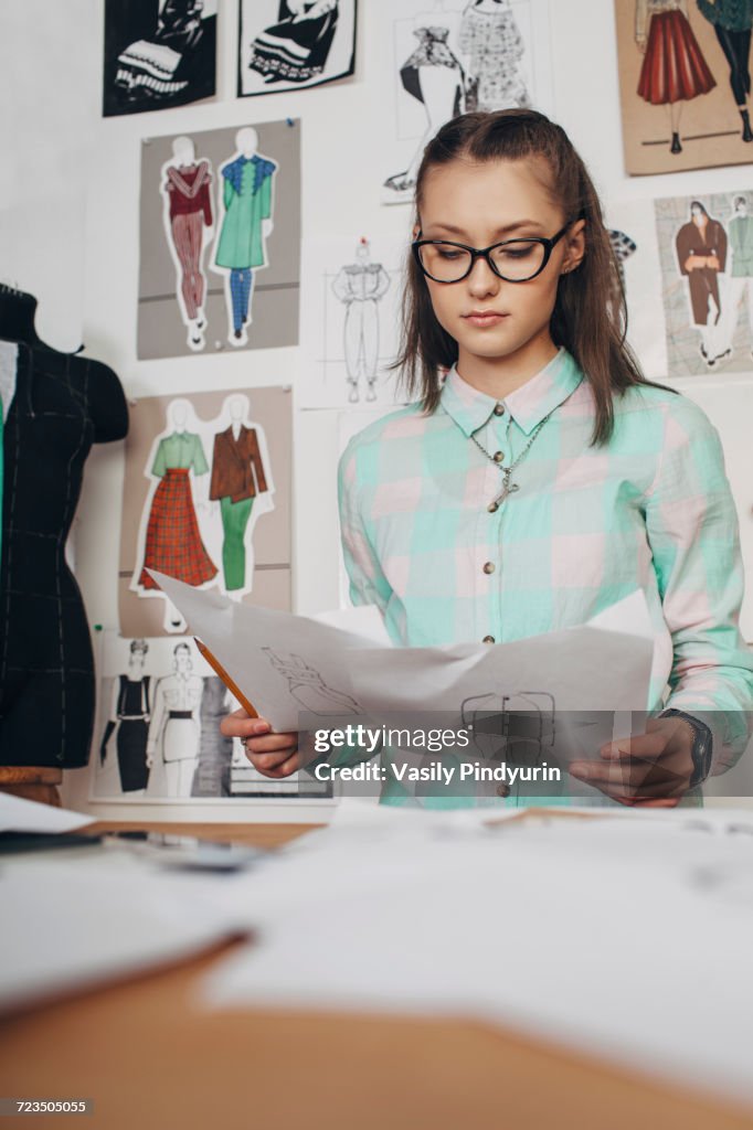 Beautiful Fashion Designer Looking At Sketches Workbench In Studio High beautiful-fashion-designer-looking-at-sketches-workbench-in-studio-high