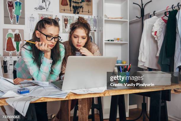 female trainee and beautiful fashion designer using laptop on workbench at design studio - design occupation fotografías e imágenes de stock