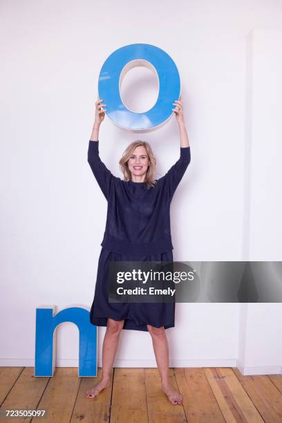 portrait of mid adult woman, holding three-dimensional letter o, next to letter n on floor - assertive stockfoto's en -beelden