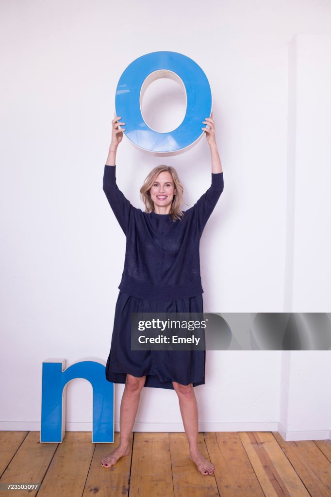 Portrait of mid adult woman, holding three-dimensional letter O, next to letter N on floor