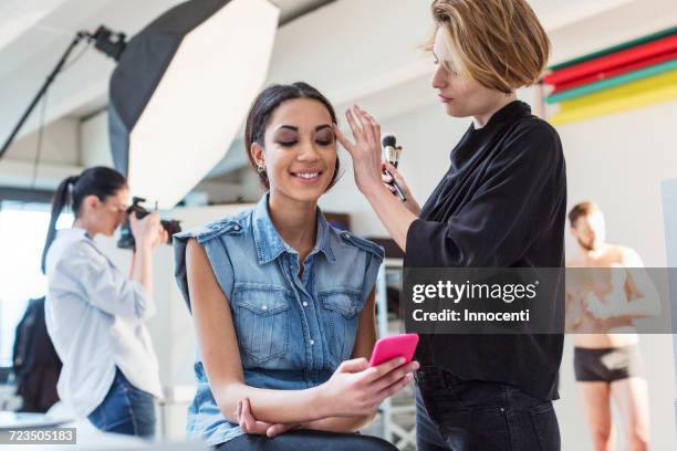make up artist applying eye shadow to model in photography studio - maquillador fotografías e imágenes de stock