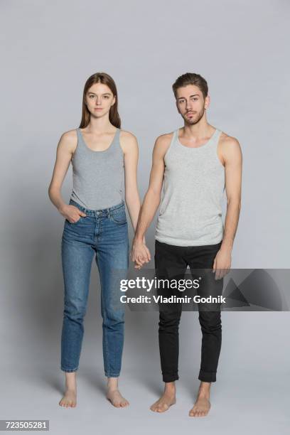 portrait of couple holding hands while standing against gray background - camiseta de tirantes fotografías e imágenes de stock