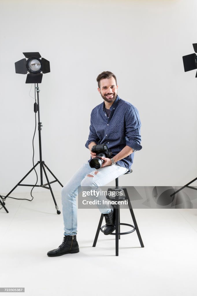 Portrait of male photographer sitting on white background in photographers studio