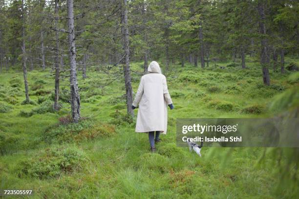 Rear view of woman wearing long coat while walking with cat on grassy field