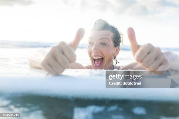 woman with surfboard in sea giving thumbs up, nosara, guanacaste province, costa rica - nosara costa rica stock pictures, royalty-free photos & images