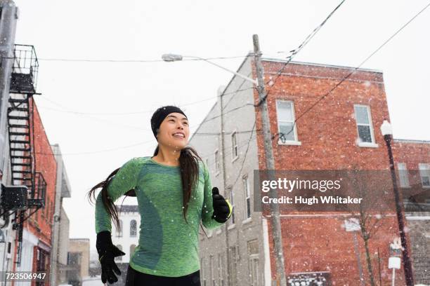 happy young female runner in knit hat running in snowy street - happy people running stockfoto's en -beelden