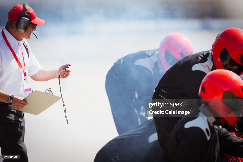 Manager with stopwatch timing open-wheel single-seater racing car pit crew practice session