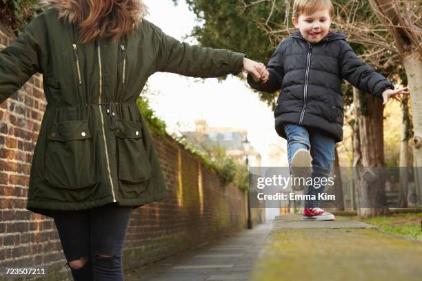 woman holding toddler sons hand walking on street wall - parka stock pictures, royalty-free photos & images