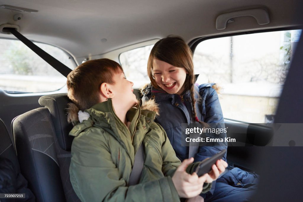 Boy and sister laughing in car backseat