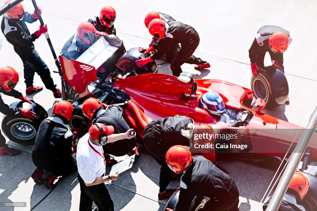 Manager with stopwatch timing pit crew replacing tires in pit lane