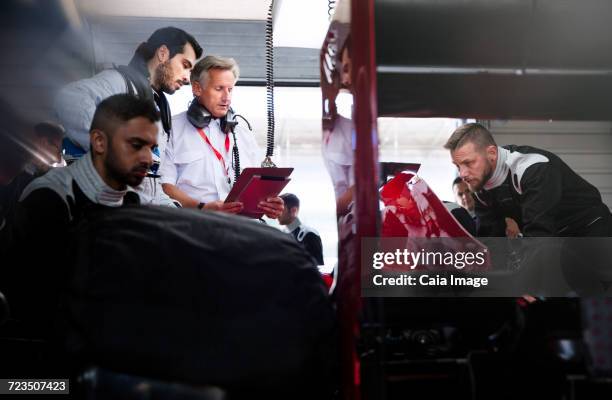 manager and driver talking behind pit crew working on race car in repair garage - auto racing stock pictures, royalty-free photos & images