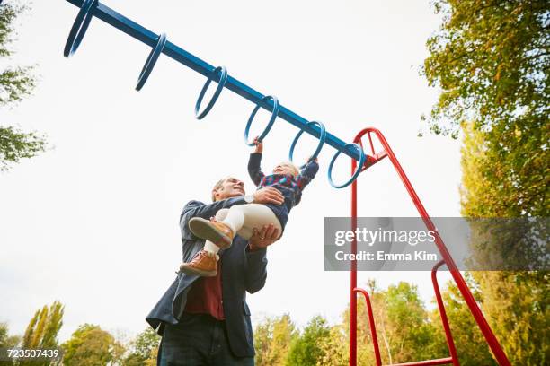 father helping daughter on monkey bars in playground - monkey bars fotografías e imágenes de stock