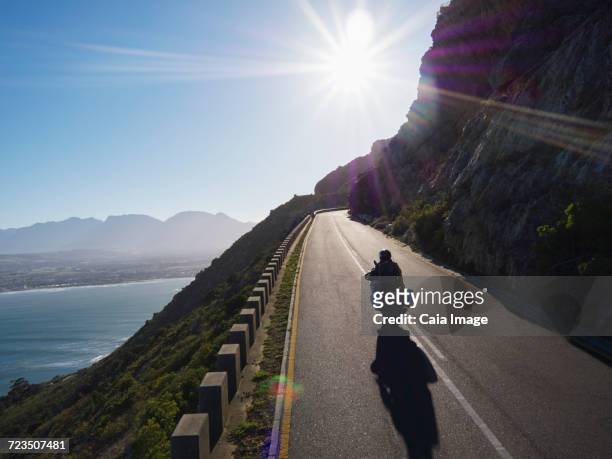 Couple riding motorcycle on sunny road along ocean