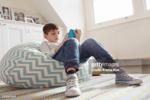 boy reclining on beanbag chair looking at digital tablet - bean bags fotografías e imágenes de stock