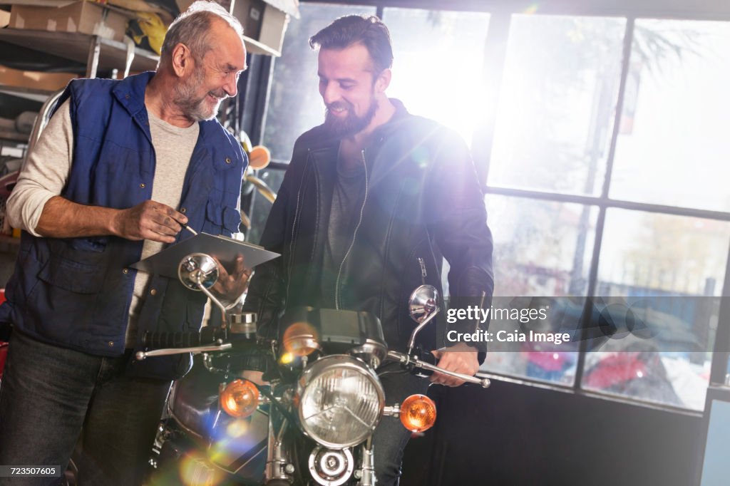 Motorcycle mechanic discussing paperwork with customer in shop