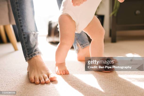 mother and babys bare feet on carpet in living room - learning to walk stockfoto's en -beelden