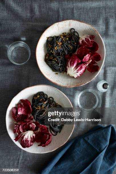 overhead view of squid ink spaghetti dish and radicchio lettuce salad - squid ink pasta stock pictures, royalty-free photos & images