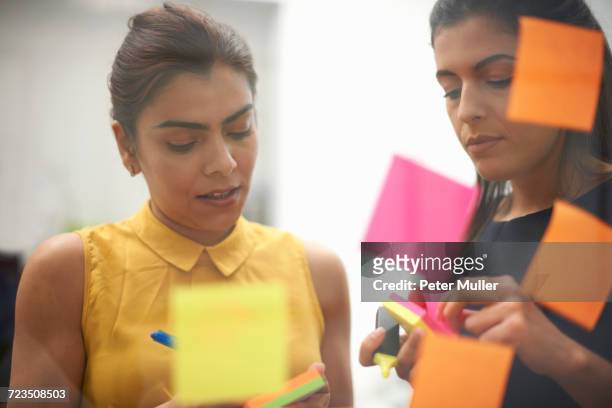 two businesswomen writing on sticky notes for office glass wall - camicetta arancione foto e immagini stock