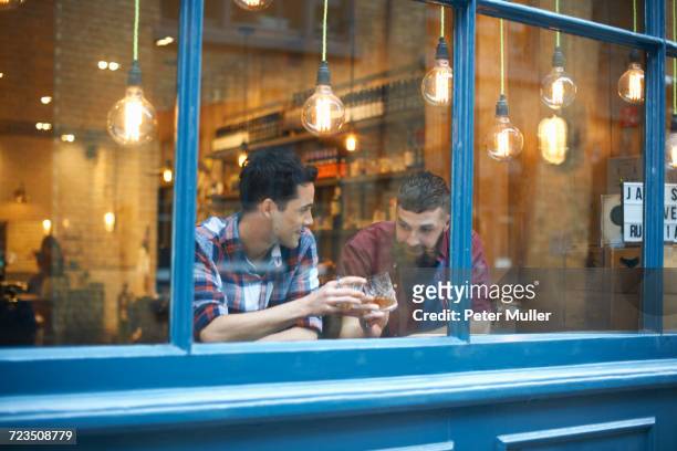 window view of two men raising a glass in public house - british pub stock-fotos und bilder