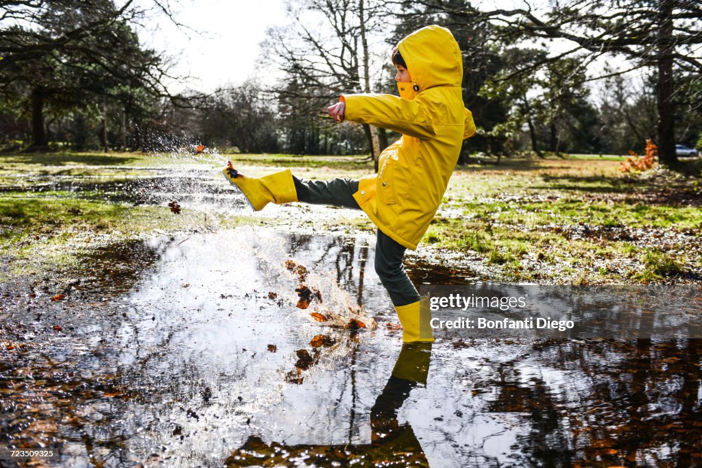Boy in yellow anorak splashing in park puddle