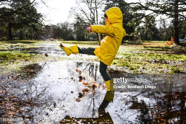 boy in yellow anorak splashing in park puddle - kids splashing stock pictures, royalty-free photos & images