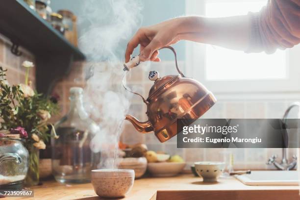arm of man pouring boiling water into bowl in kitchen - ketel stockfoto's en -beelden