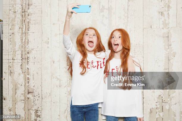 portrait of twin sisters wearing christmas jumpers, taking selfie using smartphone - twins stock pictures, royalty-free photos & images