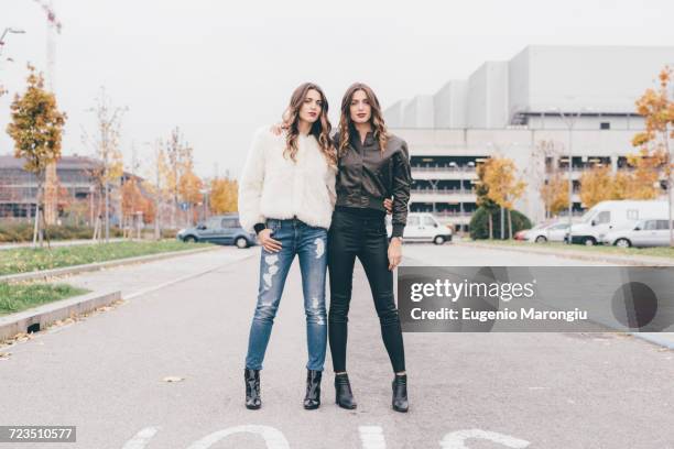 portrait of twin sisters, in urban area, standing side by side - identical twin stock pictures, royalty-free photos & images