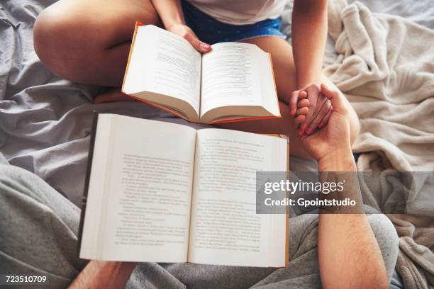 couple sitting on bed, holding books, holding hands, low section - romance book stock pictures, royalty-free photos & images