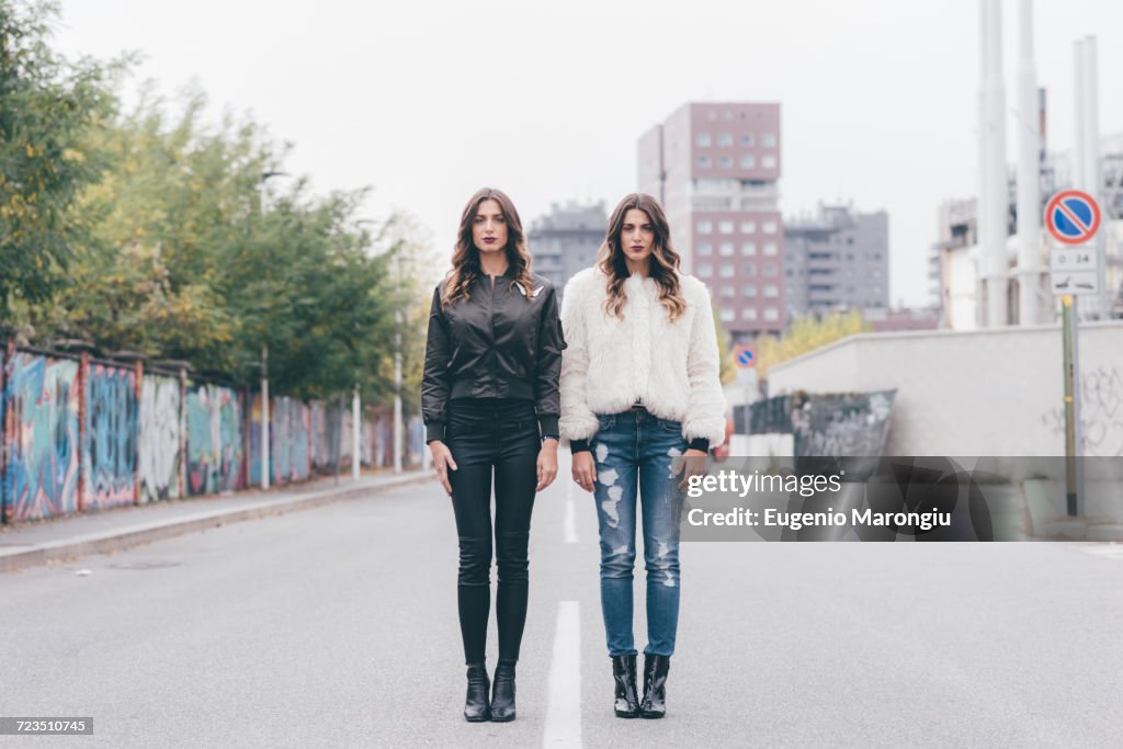 Portrait of twin sisters, in urban area, standing side by side