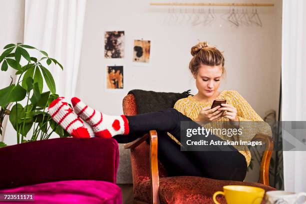 woman using phone while resting on chair at home - chignon fotografías e imágenes de stock