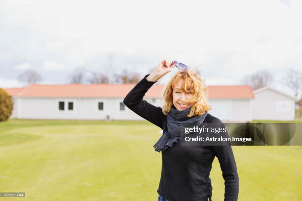 Portrait of cheerful woman removing sunglasses at golf course