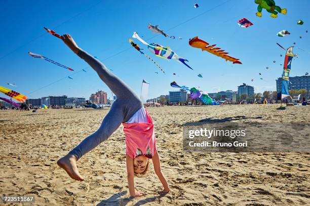 young girl doing cartwheel on beach, kites flying in sky behind her, rimini, italy - cartwheel stock pictures, royalty-free photos & images