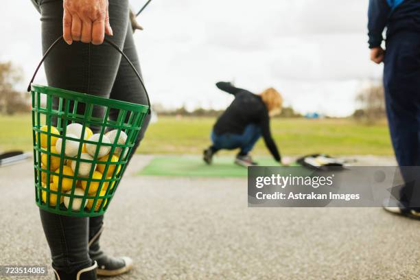 low section of woman holding basket with balls at golf course - drivingrange stockfoto's en -beelden