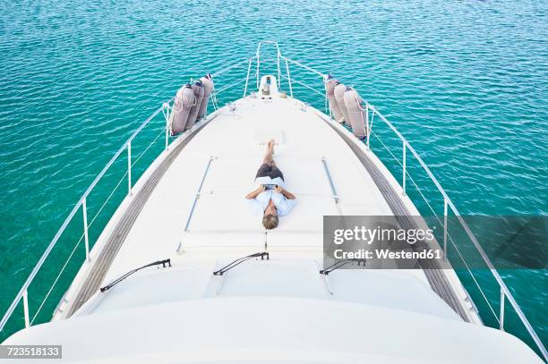 smiling man lying on deck of his motor yacht using tablet - motor yacht stock pictures, royalty-free photos & images