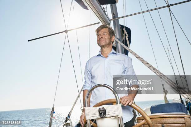 mature man at helm of his sailing boat - boat helm stock pictures, royalty-free photos & images