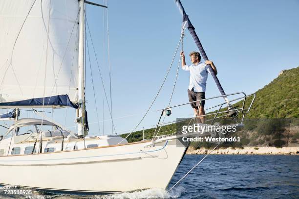 man standing on bow of his sailing boat looking at distance - ships bow stock pictures, royalty-free photos & images