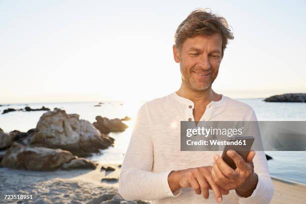 portrait of smiling man using cell phone on the beach - smartphone strand stock-fotos und bilder