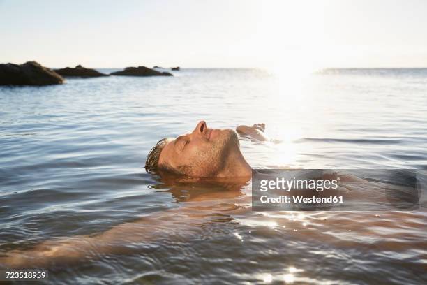 relaxed mature man floating in the sea - beach holiday stock-fotos und bilder