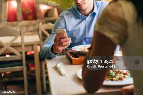 man checking messages while having dinner in a restaurant - dinner date stock pictures, royalty-free photos & images